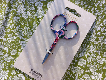 Scissors with floral handle on a branded packaging against a floral background