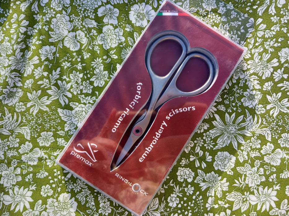 Package of embroidery scissors on a floral fabric background